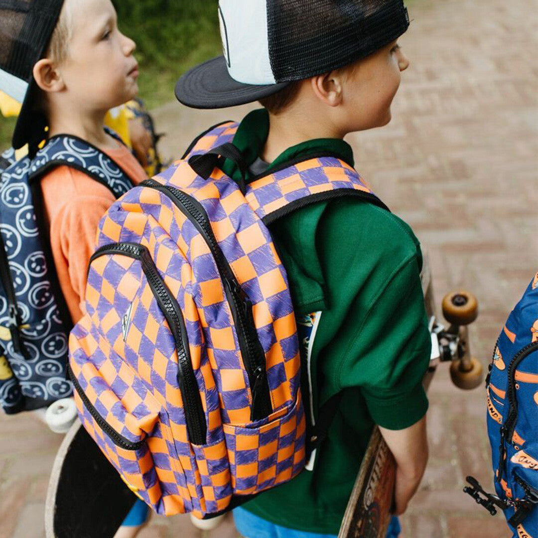 Kind draagt de Little Legends kinderrugzak met oranje en paars checkerboard patroon, schuin van achteren gezien.