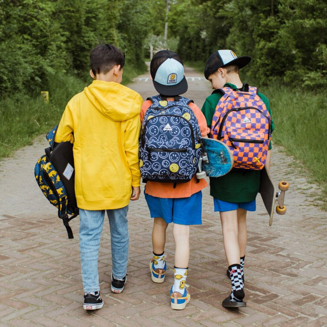 Drie kinderen lopen weg, één draagt de Little Legends kinderrugzak met oranje en paars checkerboard patroon.