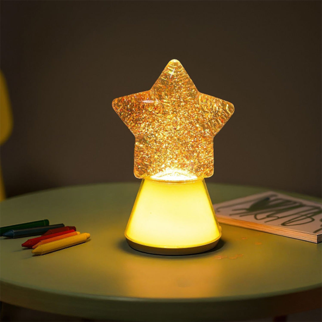 Het Little L ster nachtlampje geeft warm geel licht op een tafel met kleurpotloden.