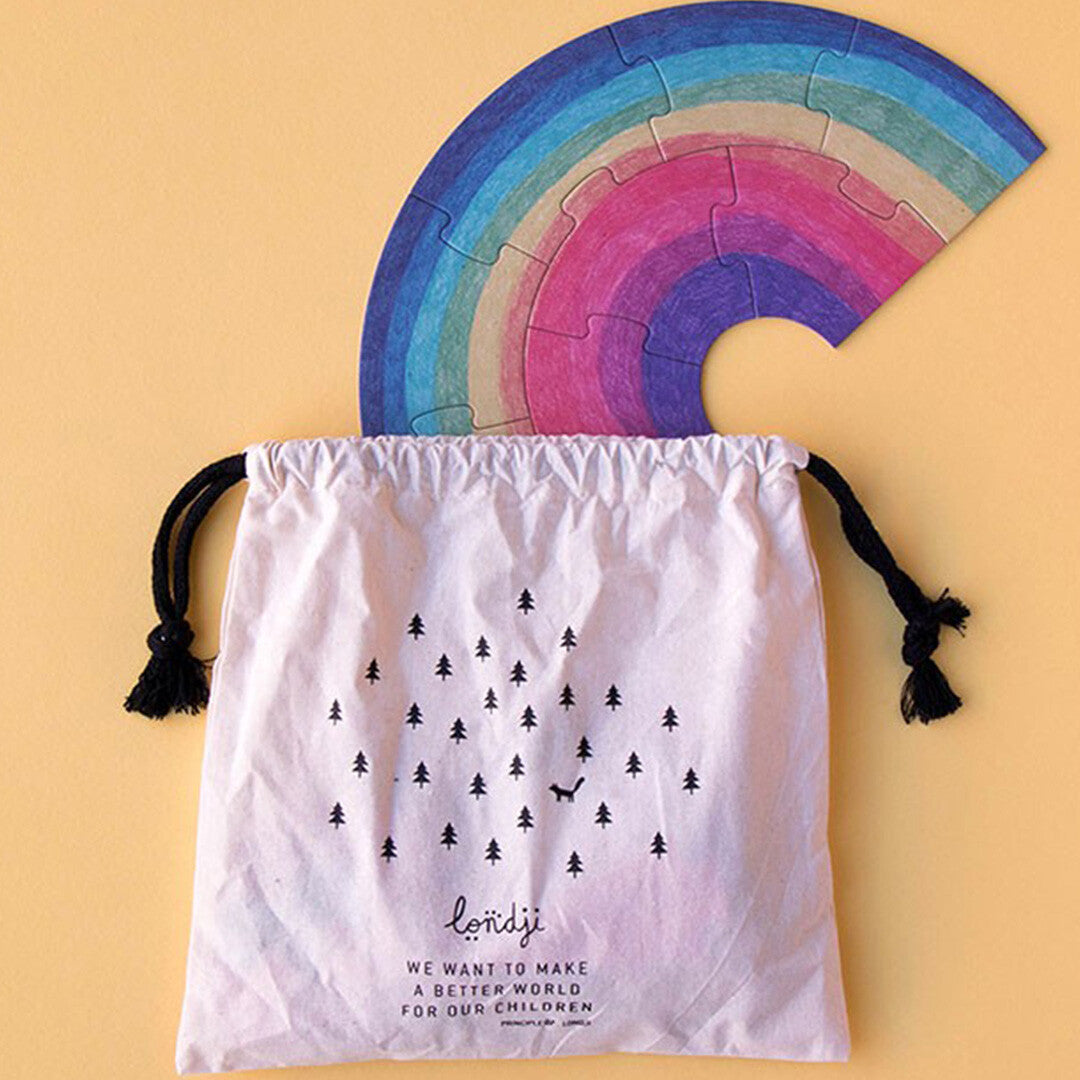 Een witte londji opbergzak met bosprint waar een regenboog legpuzzel uitsteekt.