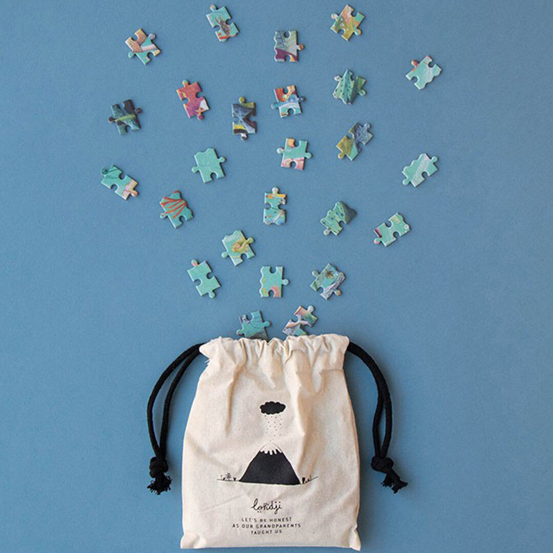 Losse puzzelstukjes van de Londji legpuzzel die uit een stoffen opbergzakje vallen.