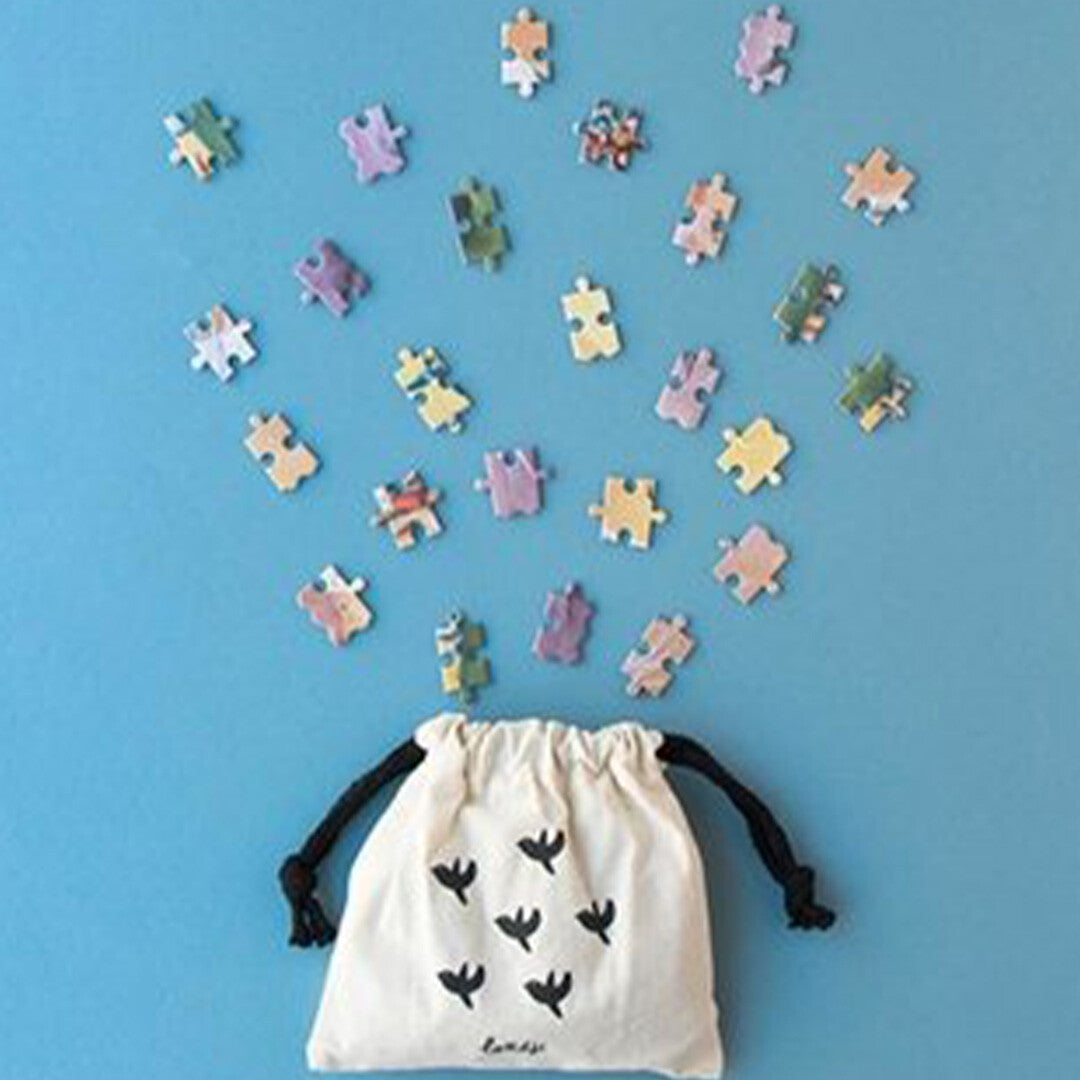 Verspreide puzzelstukjes van de londji My Unicorn legpuzzel die uit een wit stoffen zakje lijken te komen.