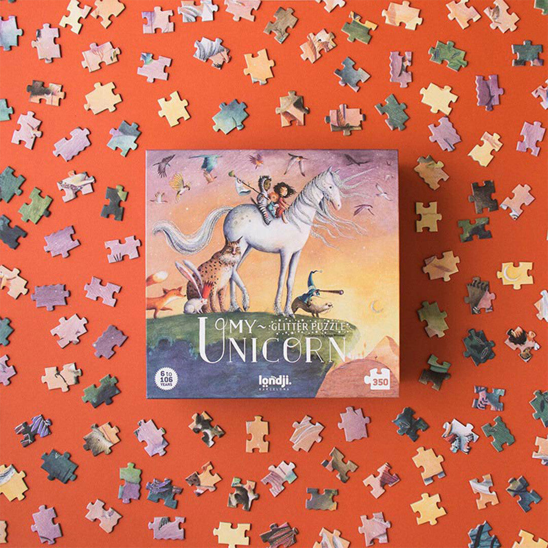 De Londji My Unicorn legpuzzelverpakking omringd door losse puzzelstukjes op een oranje ondergrond.