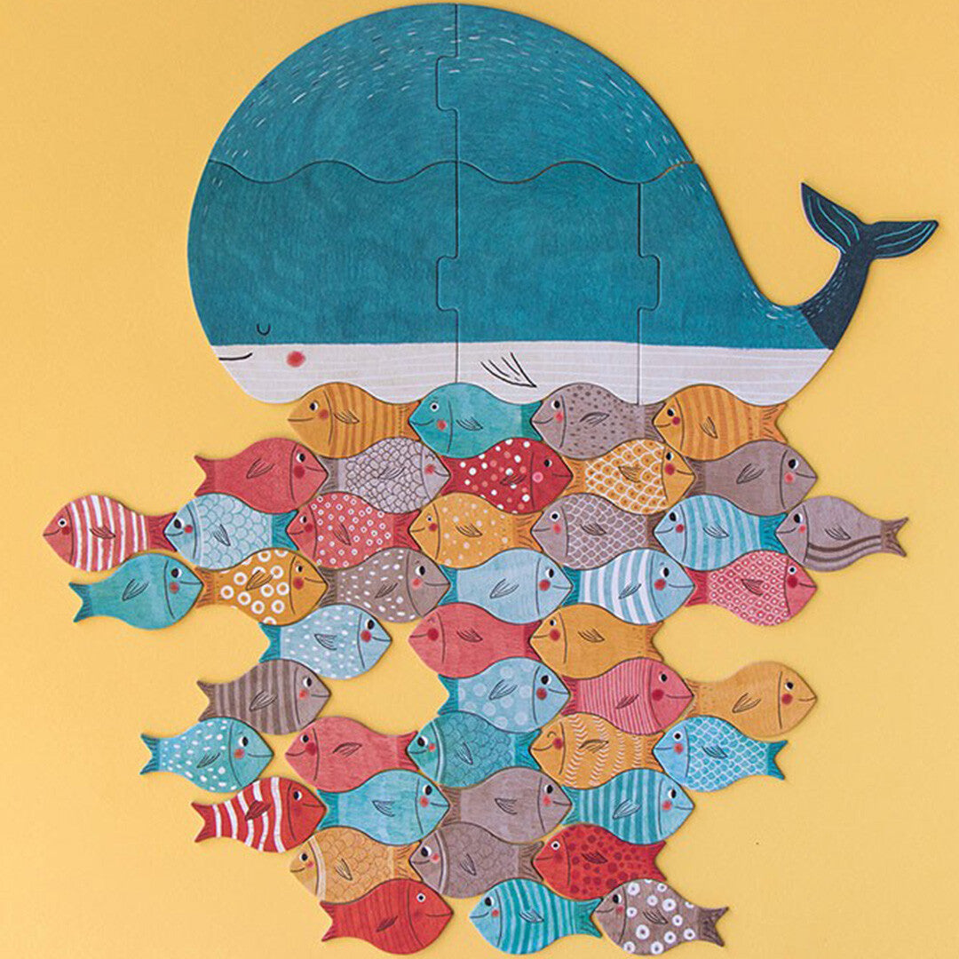 Voltooide legpuzzel van een blauwe walvis met daaronder een groep kleurrijke vissen op een gele achtergrond.