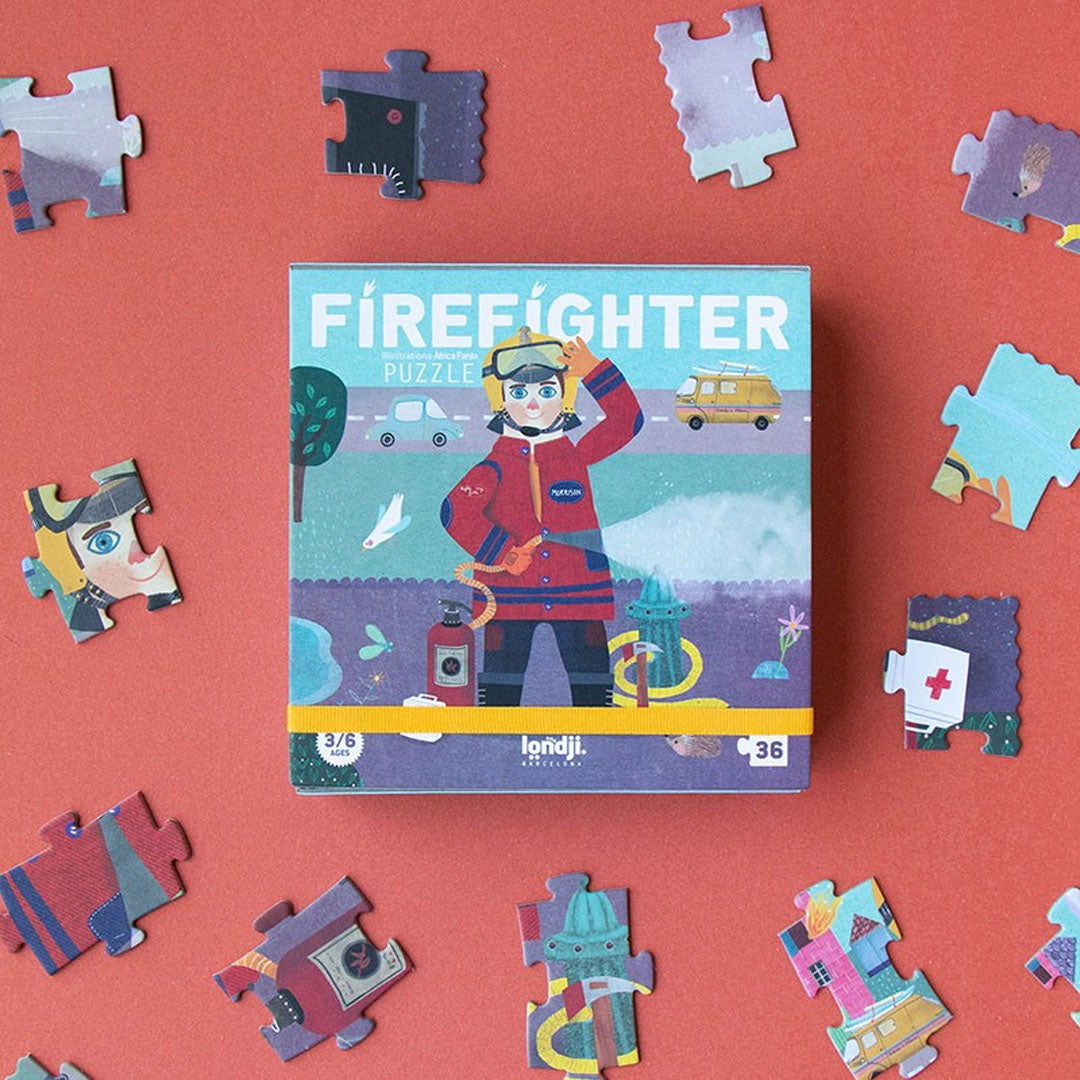 De Londji 'Firefighter' legpuzzelverpakking omringd door losse puzzelstukjes op een rode achtergrond.