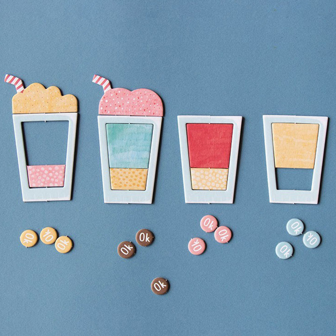 Vier lege witte milkshakebekerframes met daarin gekleurde houten onderdelen en kleine 'OK' fiches, als demonstratie van het londji Shakes spel.
