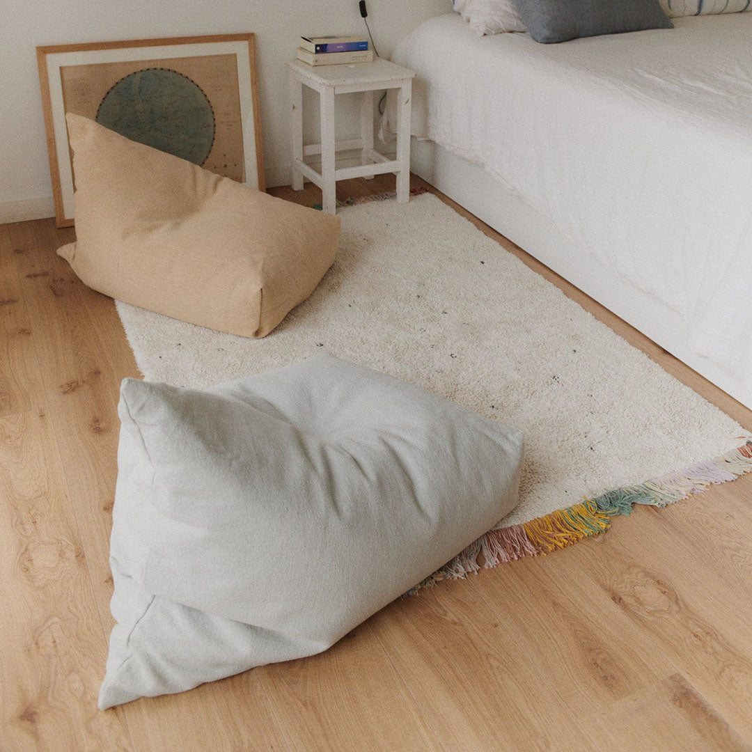 Twee Lorena Canals zitzakken, een blauwe en een beige, op een houten vloer in een slaapkamer.