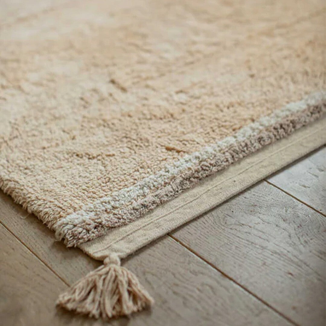 Detailopname van de textuur en kwastjes van het beige gestreepte vloerkleed op een houten vloer.
