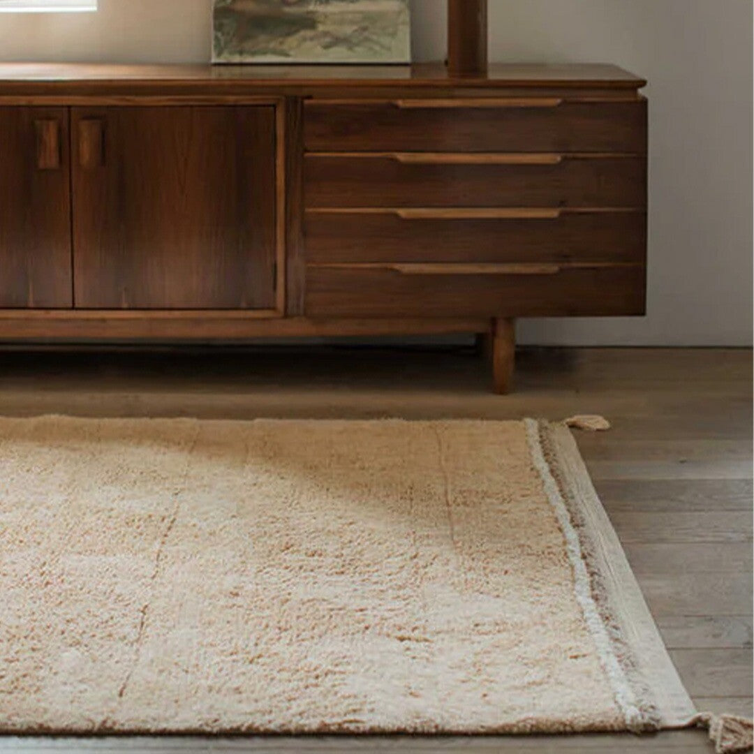 Beige gestreept vloerkleed met kwastjes op een houten vloer voor een houten dressoir.