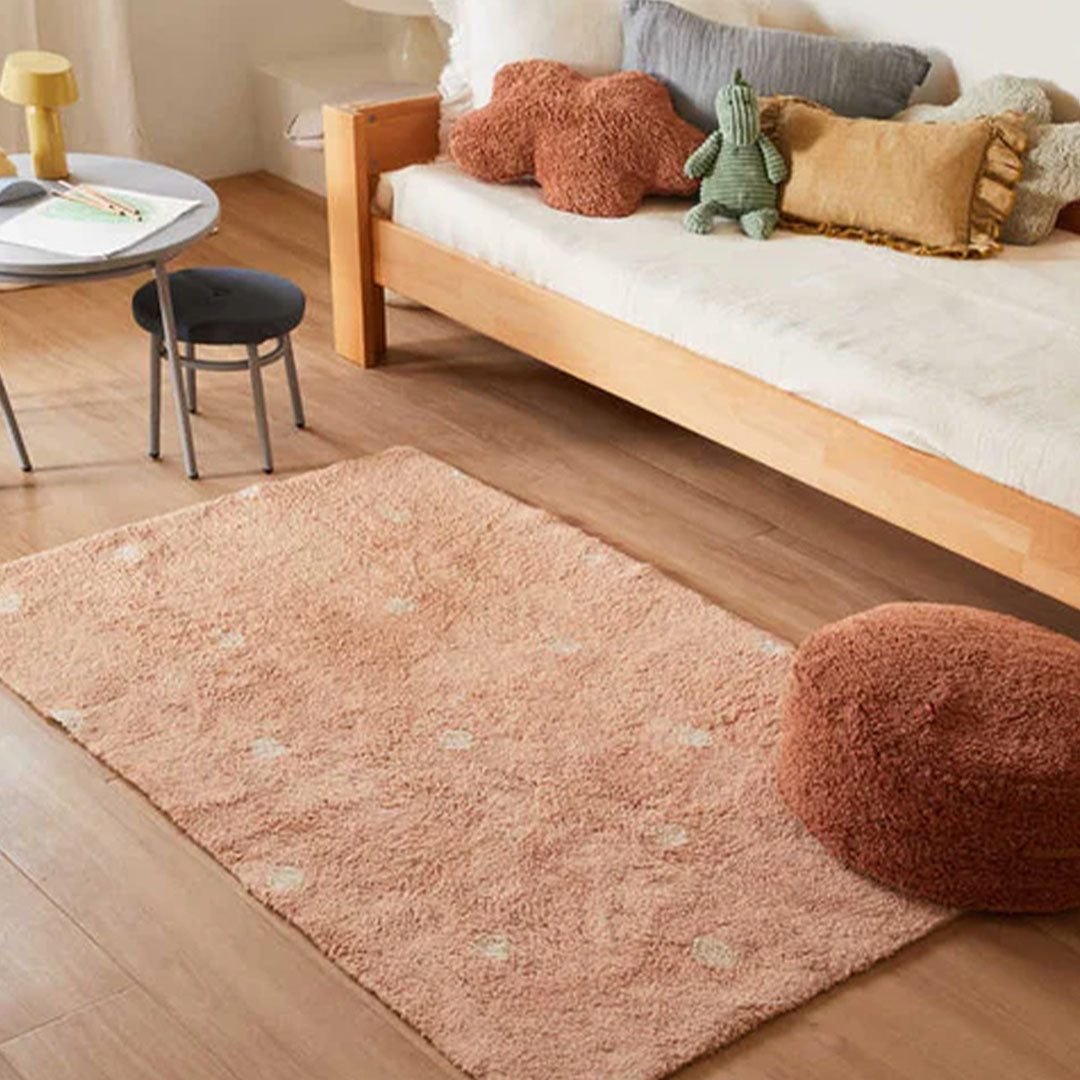Roze vloerkleed met witte stippen op een houten vloer in een kinderkamer.