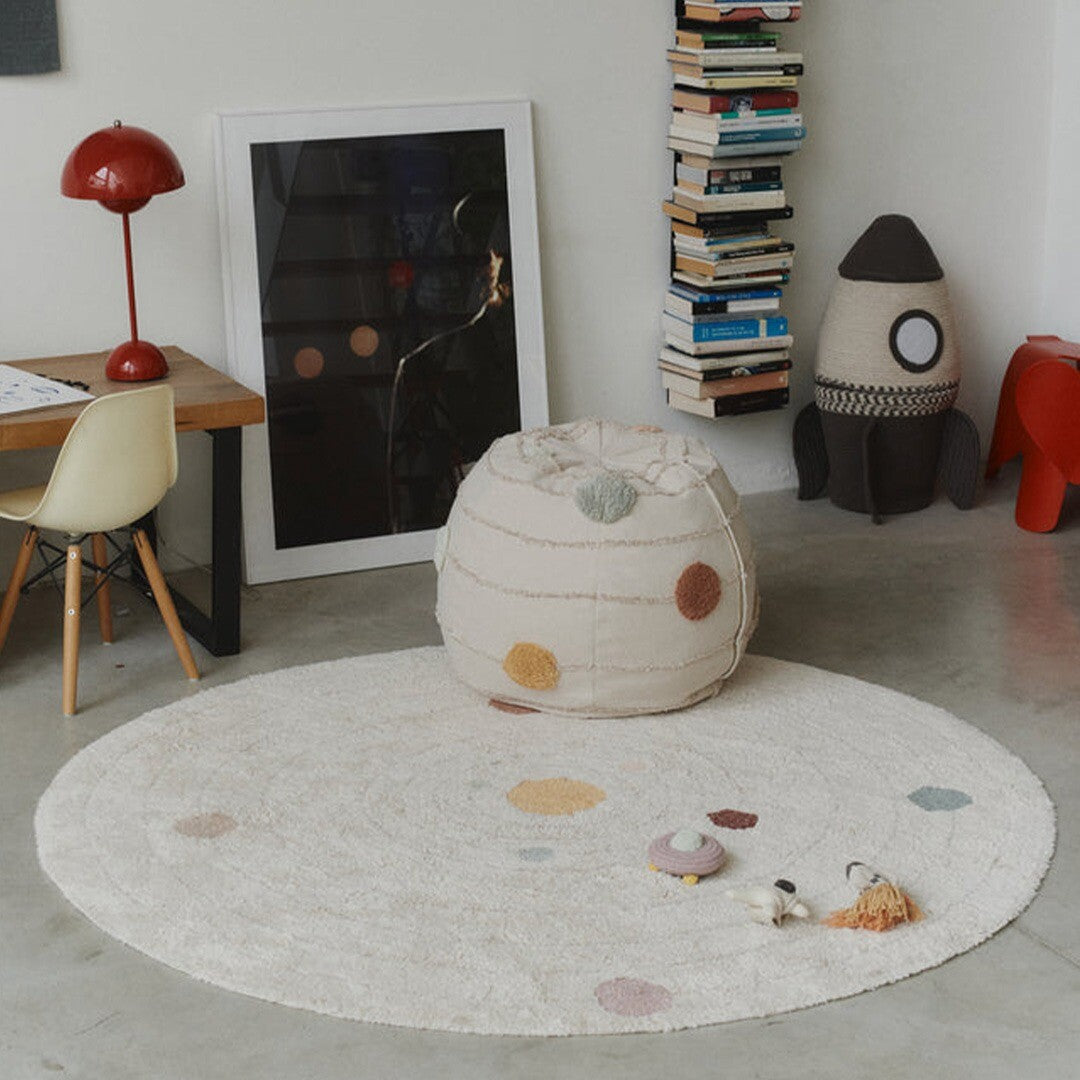 Het Lorena Canals solar system vloerkleed ligt in een kinderkamer met een bijpassende poef en raket.