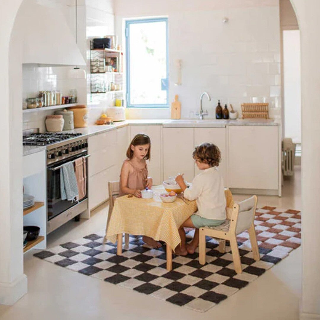 Lorena Canals vloerkleed met grijs en wit geruit patroon op de vloer in een keuken met twee spelende kinderen.