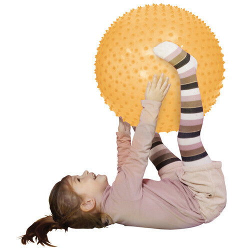 Een kind speelt met de oranje fitness bal, liggend op de rug.
