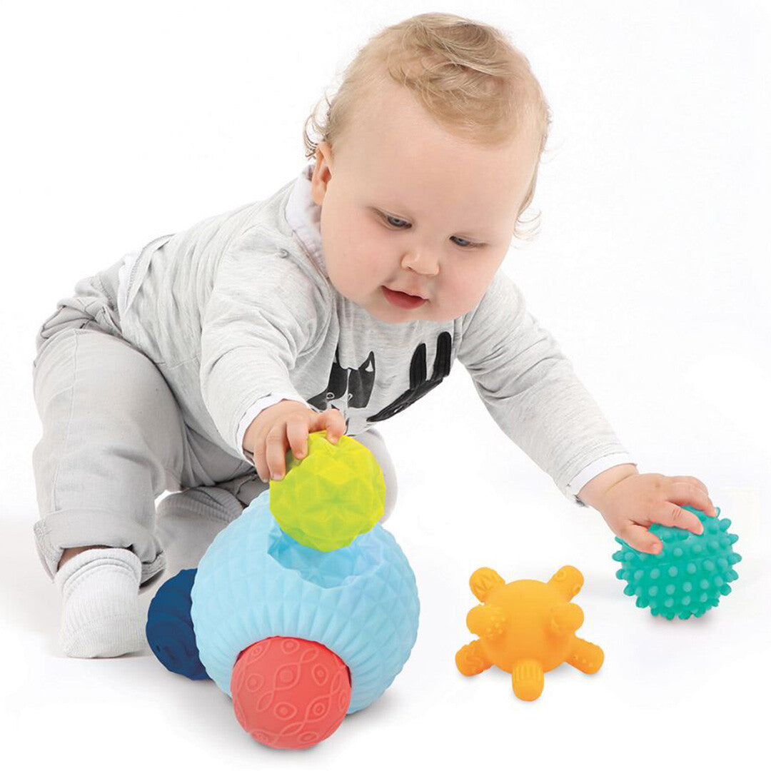 Een baby speelt met de Ludi puzzelbal, waarbij het een groen getextureerd onderdeel vasthoudt.