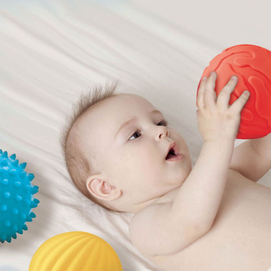 Een baby ligt op de rug en speelt met een rode Ludi sensorische bal.