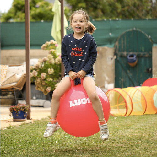 Meisje springt op een Ludi rode skippybal in de tuin.