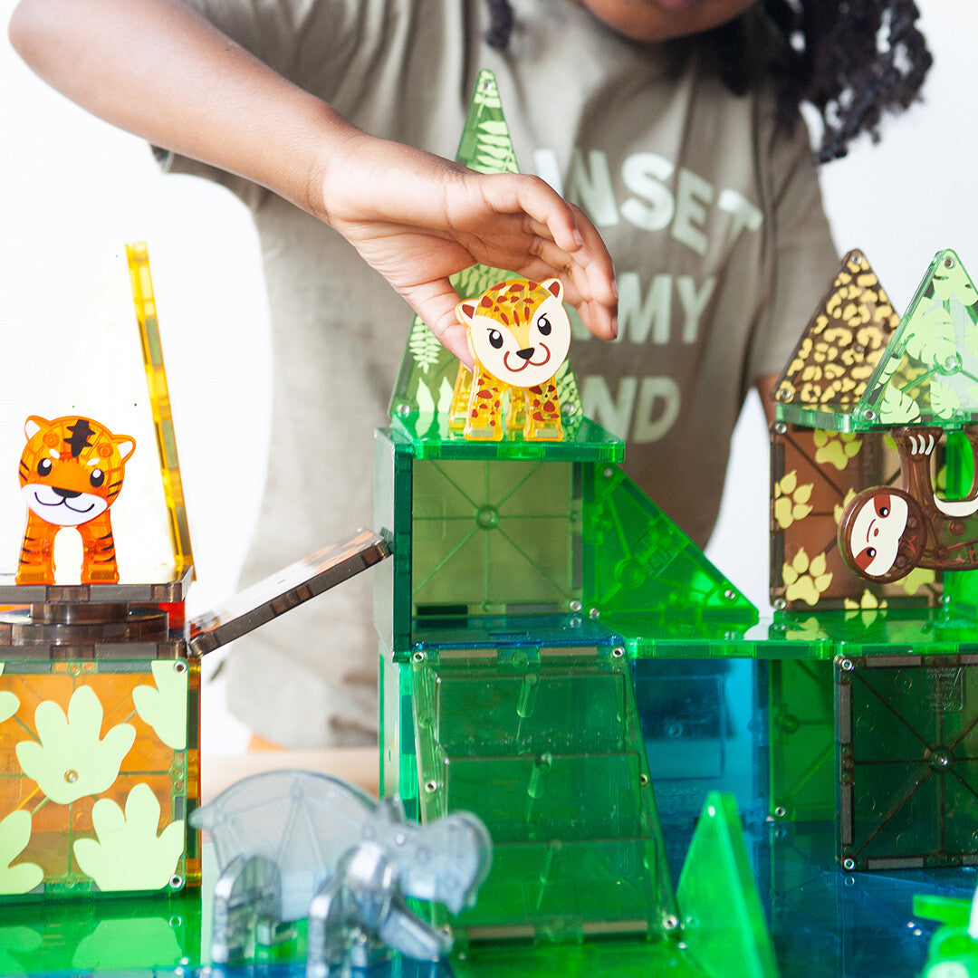 Een kinderhand plaatst een luipaardfiguur op een groene Magna-Tiles junglebouwsel.
