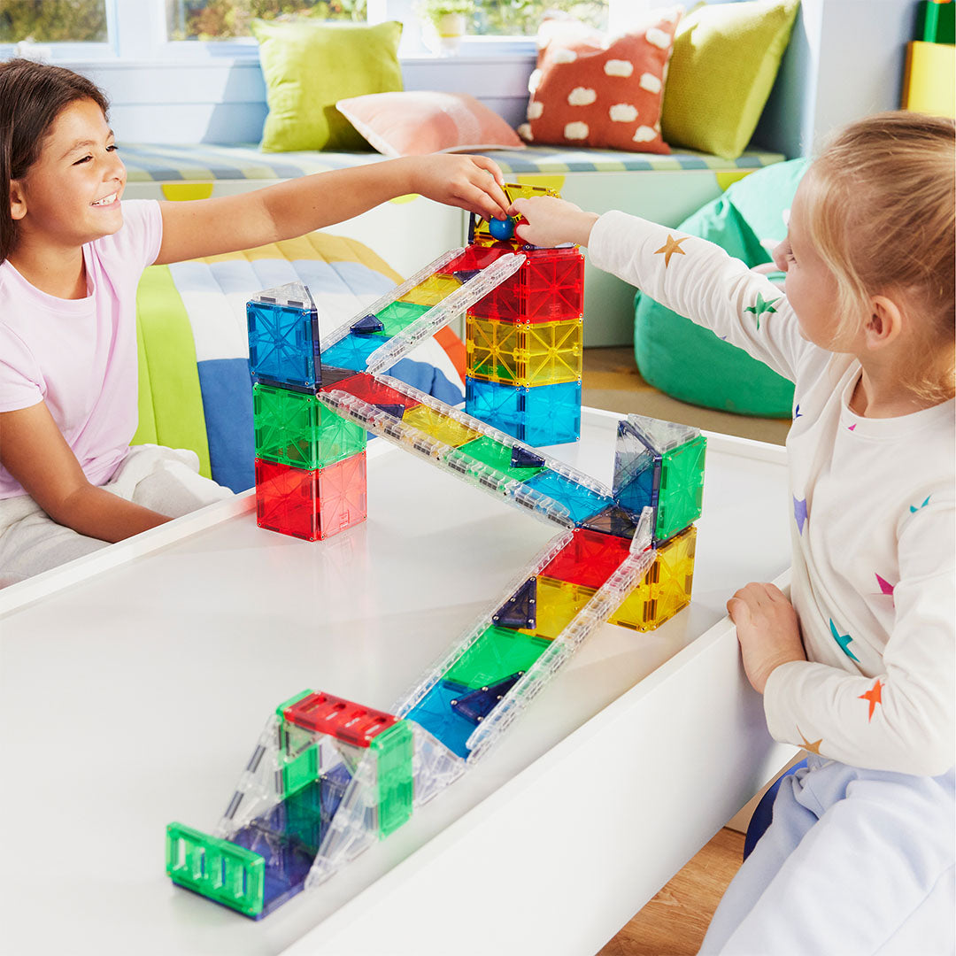 Twee kinderen spelen met de kleurrijke Magna-Tiles knikkerbaan op een witte tafel.