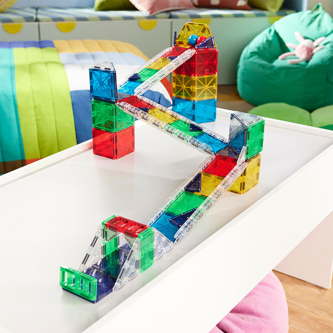 Een gebouwde Magna-Tiles knikkerbaan met een blauwe bal bovenaan op een witte tafel.