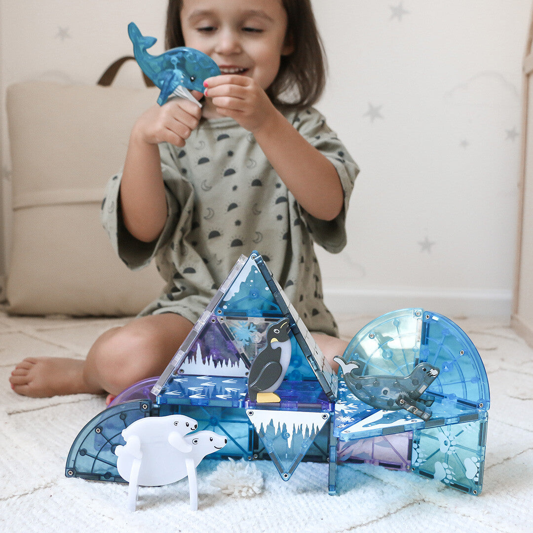 Een kind speelt met de Magna-Tiles Arctic Animals magnetische tegels en dierenfiguren op een vloerkleed.
