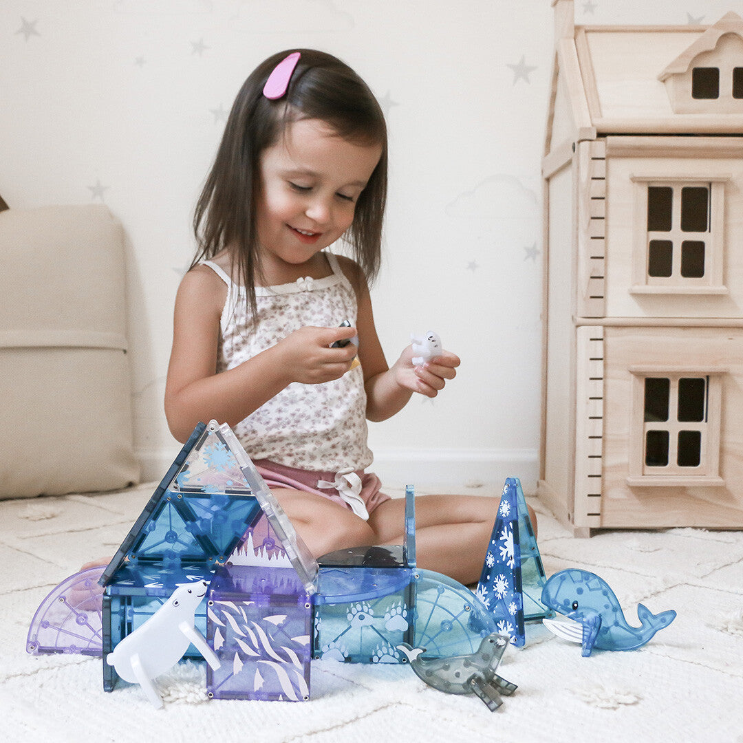 Een kind speelt met de Magna-Tiles Arctic Animals magnetische tegels en dierenfiguren naast een houten poppenhuis.