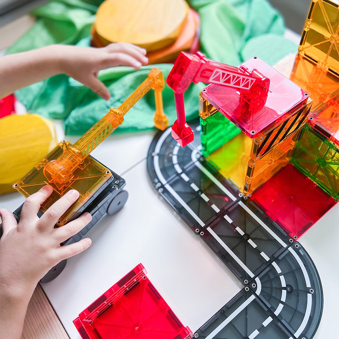 Kinderhanden spelen met de Magna-Tiles Builder magnetische tegels bouwset, inclusief kranen en wegdelen.