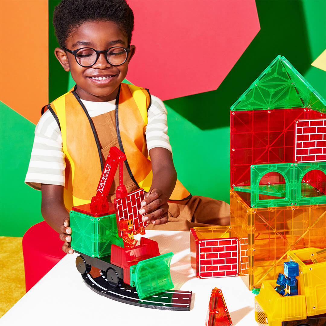 Een lachende jongen bouwt met de Magna-Tiles Builder XL magnetische tegels en plaatst een tegel op een rode kraan.