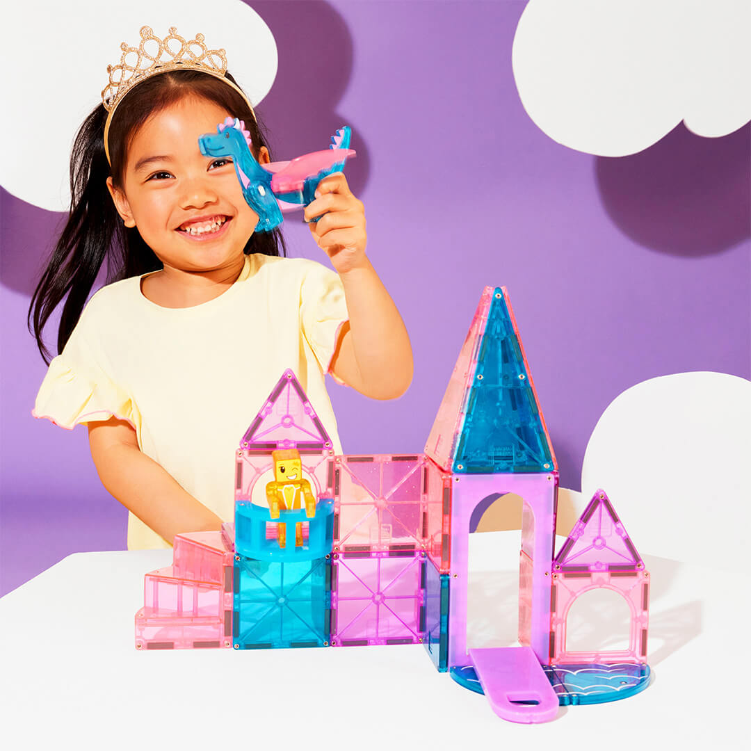 Een lachend kind met een kroontje speelt met de Magna-Tiles Castle bouwset en houdt de draak omhoog.