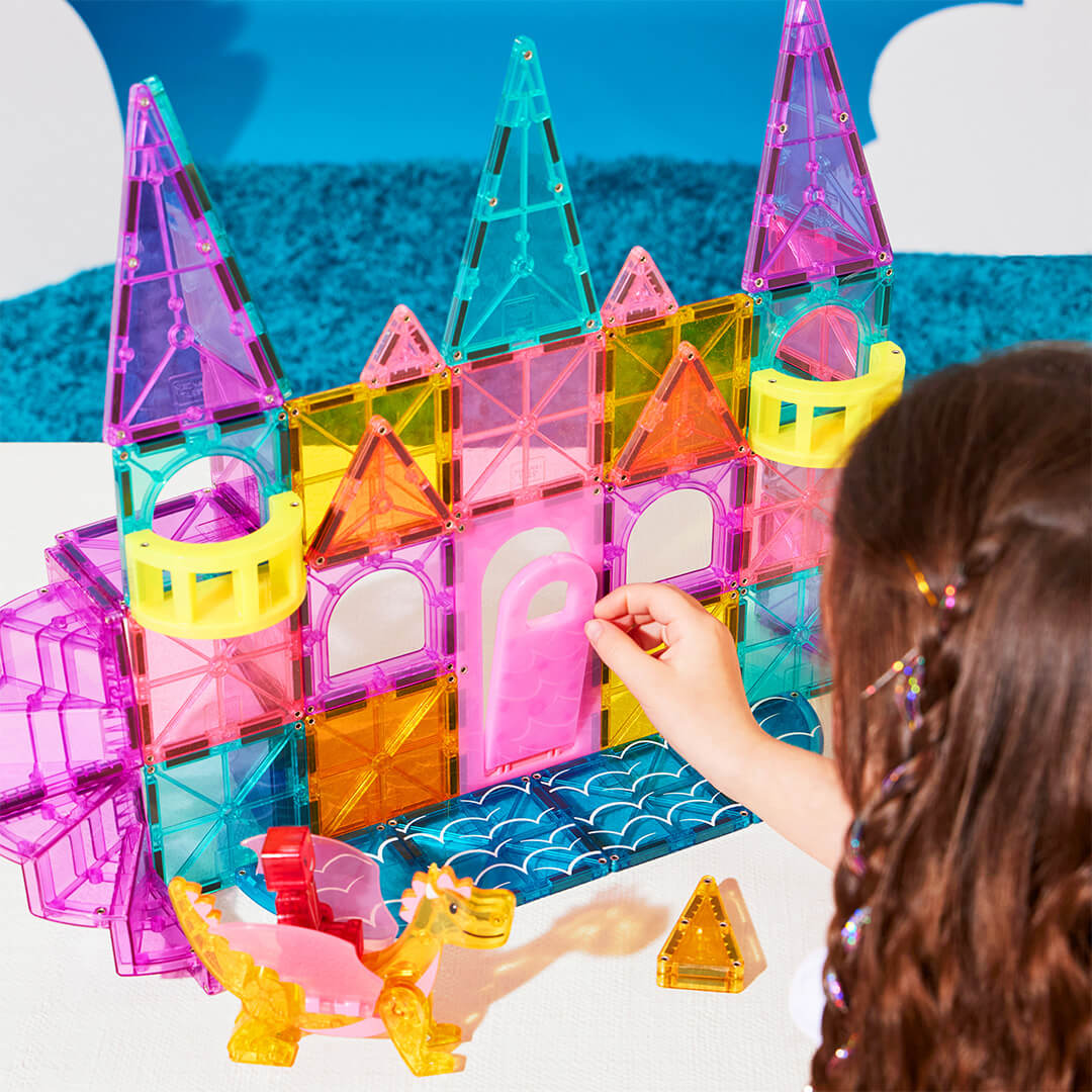 Een meisje speelt met het Magna-Tiles magnetische kasteel, waarbij haar hand een tegel vasthoudt en een draak op de voorgrond staat.