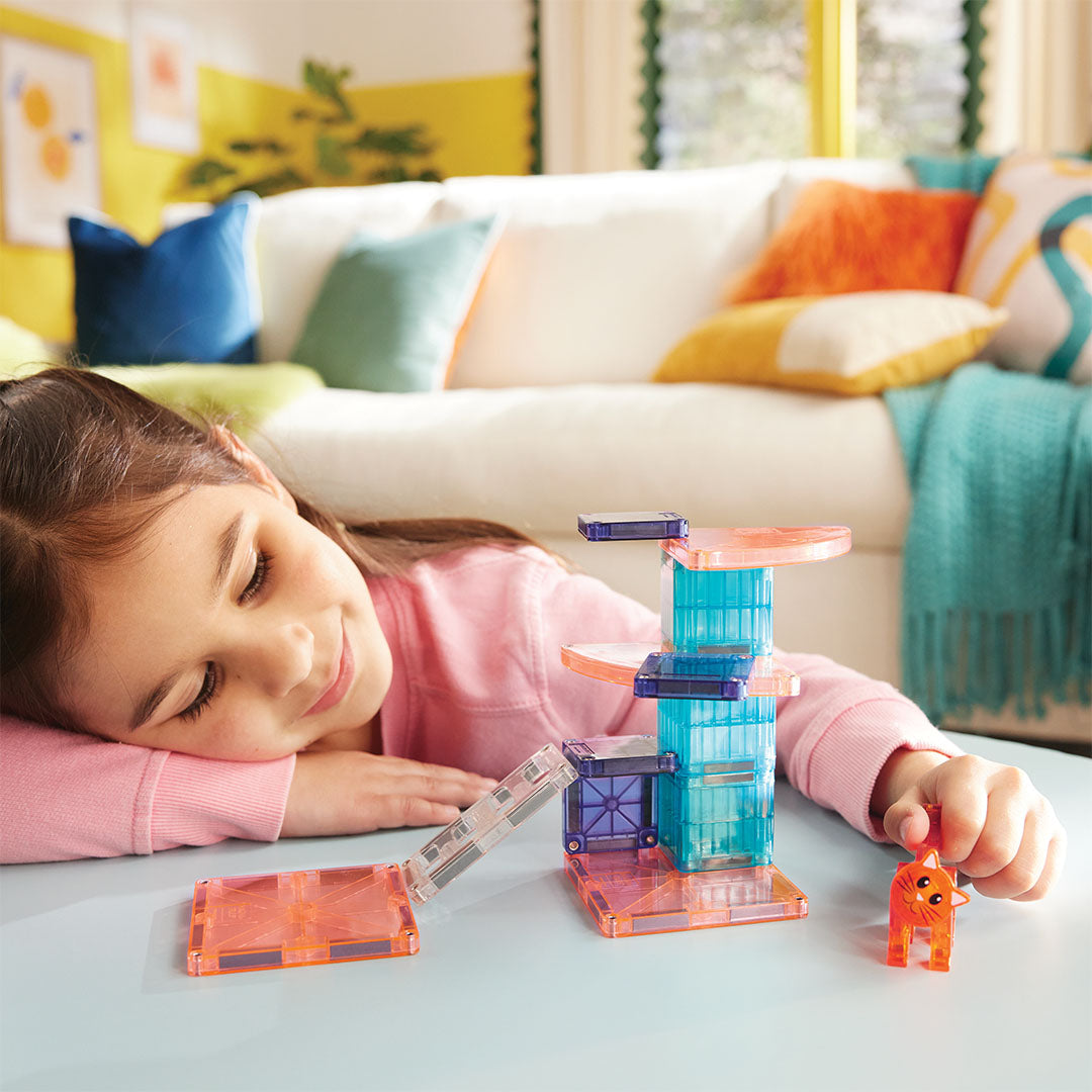 Een meisje leunt op tafel en kijkt naar de Magna-Tiles Cat Tree bouwset met het kattenfiguur.