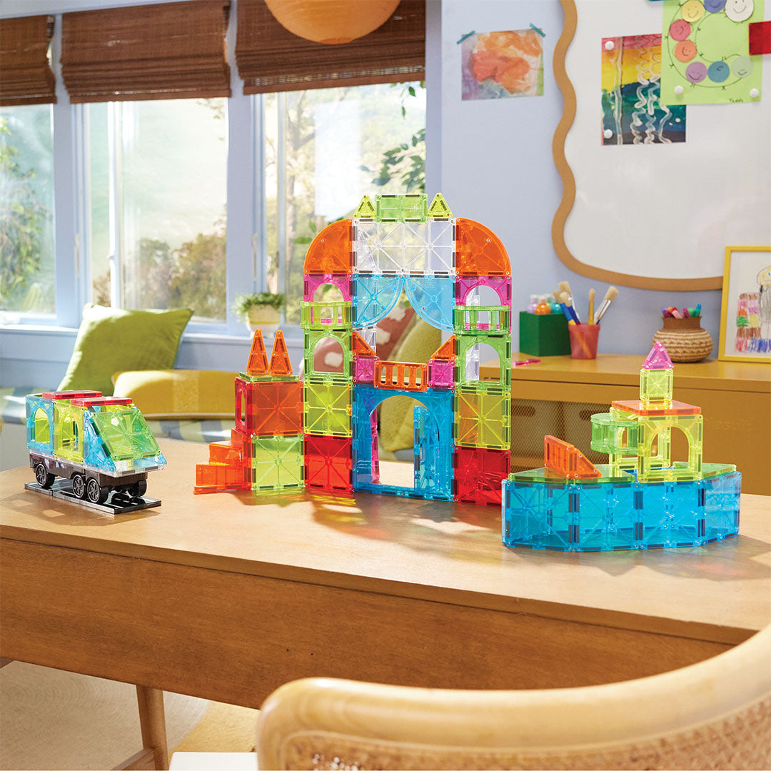 Een complete opstelling van de Magna-Tiles City Center bouwset op een houten tafel, met een groot gebouw, een trein en een kleiner gebouw.