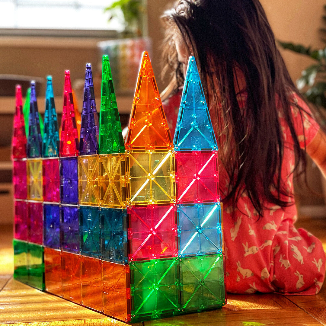 Een kind speelt met een groot, kleurrijk kasteel gemaakt van Magna-Tiles magnetische tegels.