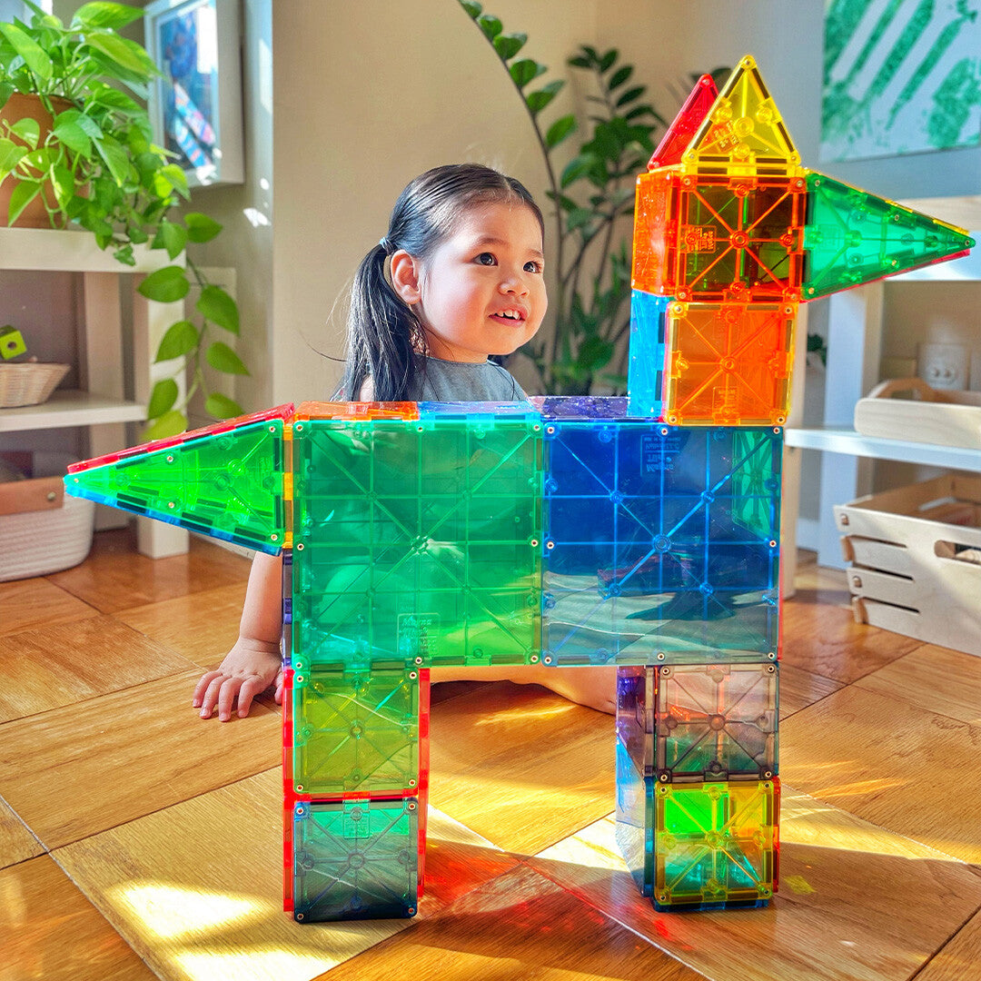 Een kind zit achter een groot, kleurrijk dier gemaakt van Magna-Tiles magnetische tegels.