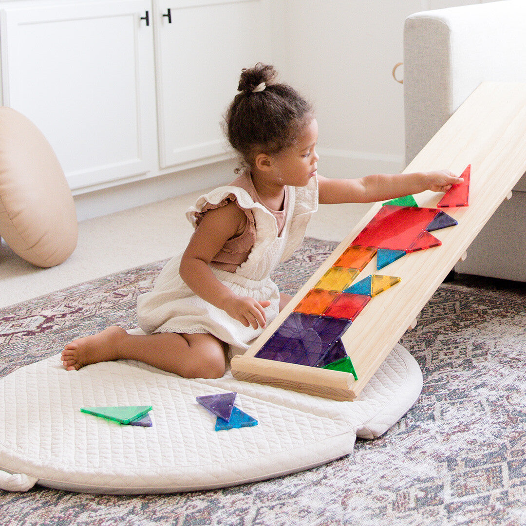 Een jong kind speelt met Magna-Tiles magnetische tegels op een houten speelhelling.