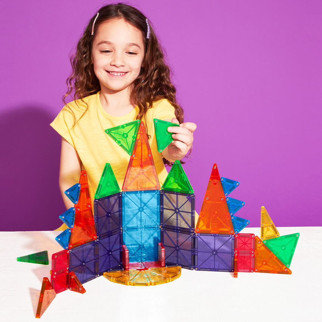 Een lachend meisje bouwt een kleurrijk kasteel met Magna-Tiles magnetische tegels.