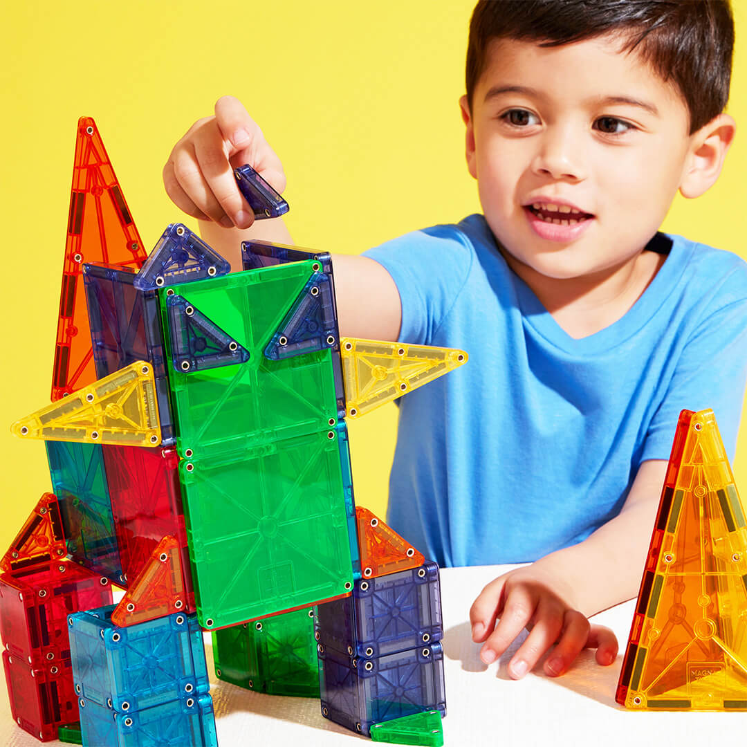Een jongetje bouwt met transparante, veelkleurige Magna-Tiles magnetische tegels een fantasiefiguur.
