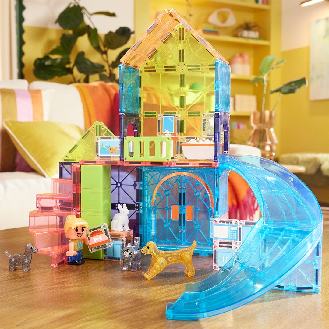De Magna-Tiles Pet Playhouse bouwset met een kleurrijk huis en dierenfiguren staat op een houten tafel in een woonkamer.