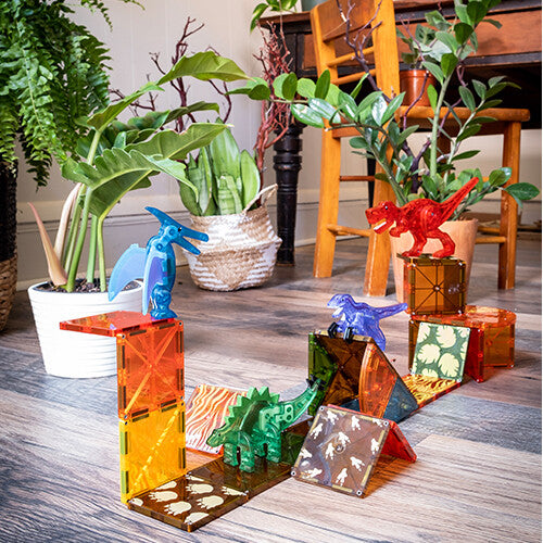 Een opstelling van Magna-Tiles Dino World magnetische tegels met verschillende dinosaurusfiguren op een houten vloer.