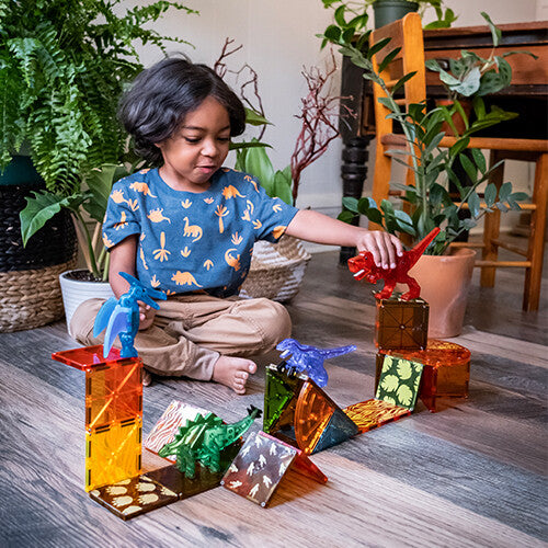 Een kind speelt op de grond met de Magna-Tiles Dino World magnetische tegels en dinosaurusfiguren.