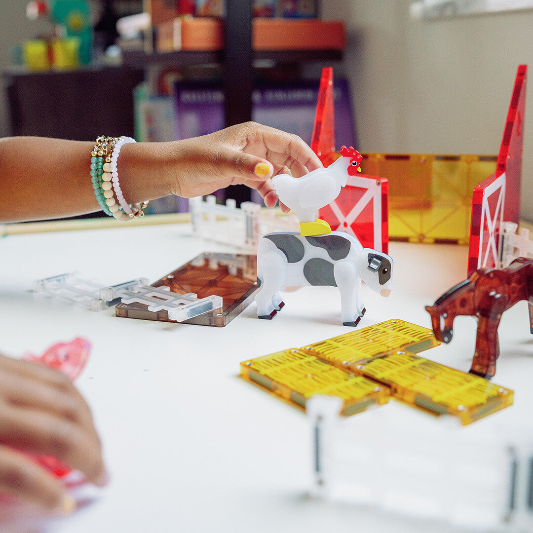 Een kinderhand plaatst een witte kip op een koe van de Magna-Tiles Farm Animals bouwset.