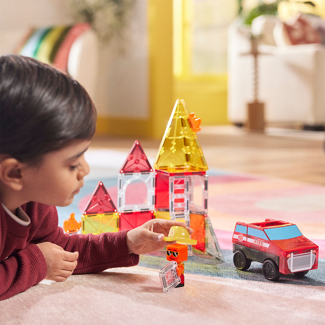 Een kind speelt op de grond met de Magna-Tiles Fire Rescue bouwset en een brandweermanfiguur.