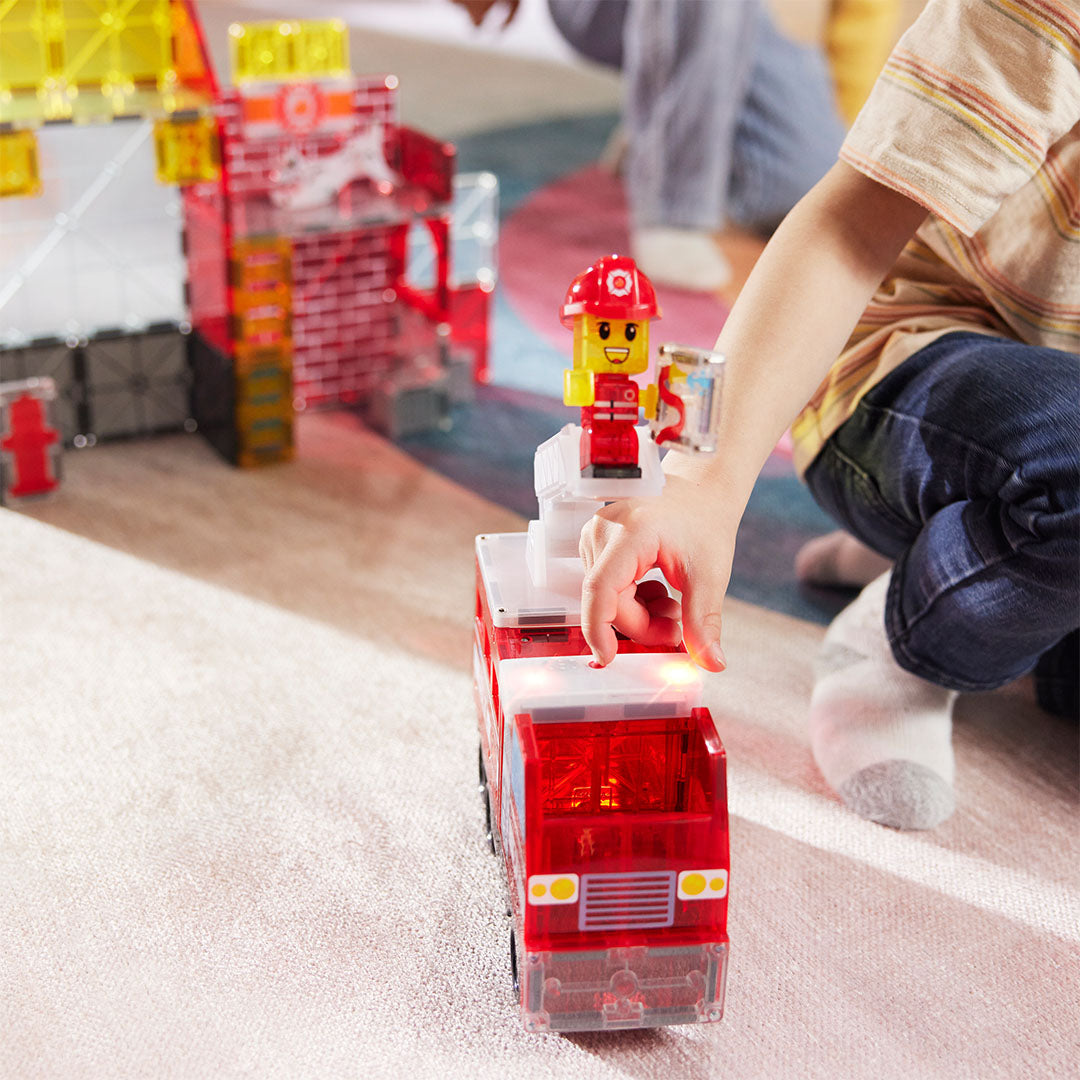 Een kinderhand drukt op de knop van de Magna-Tiles brandweerwagen met verlichting.