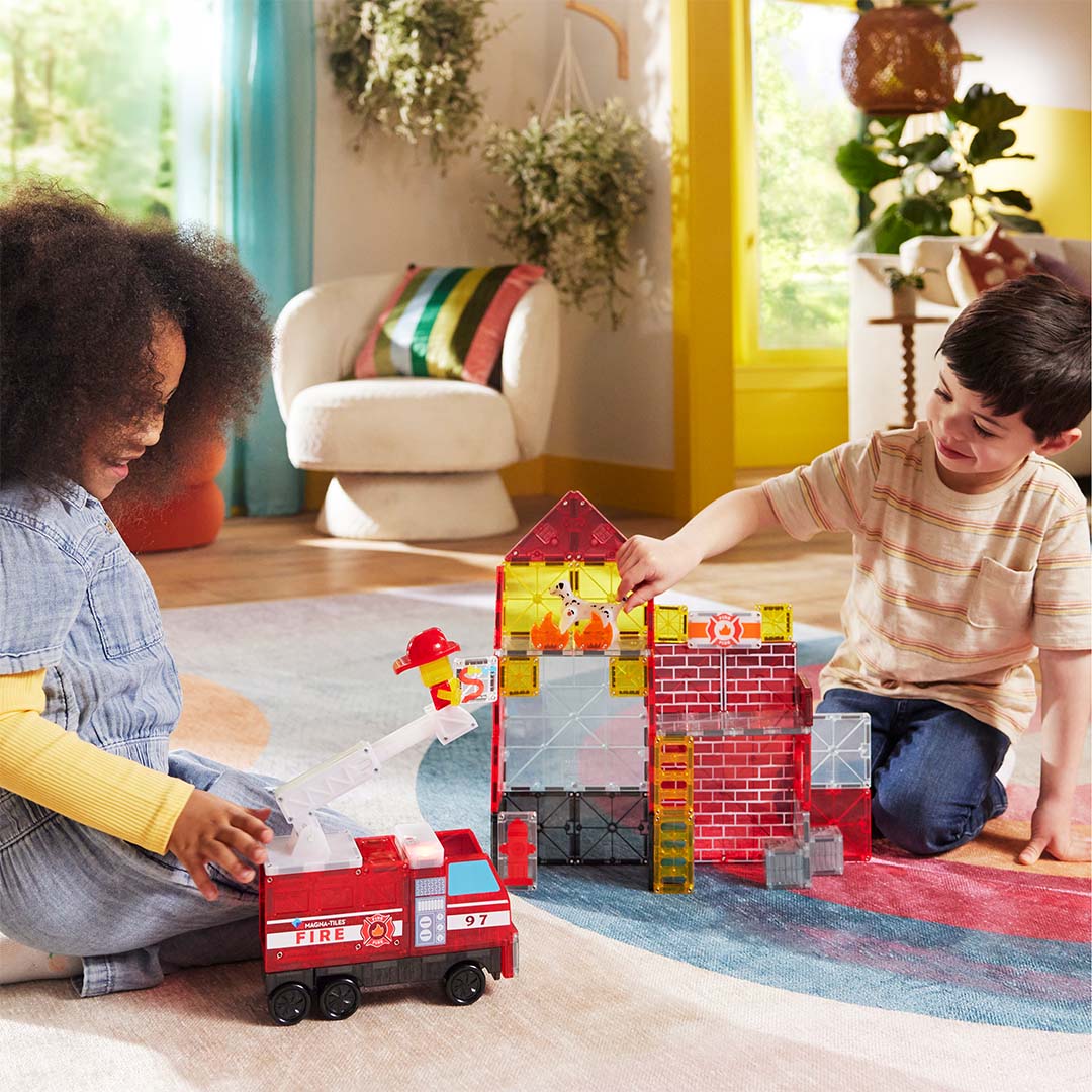 Twee kinderen spelen samen met de Magna-Tiles brandweerkazerne en brandweerwagen bouwset op een vloerkleed.
