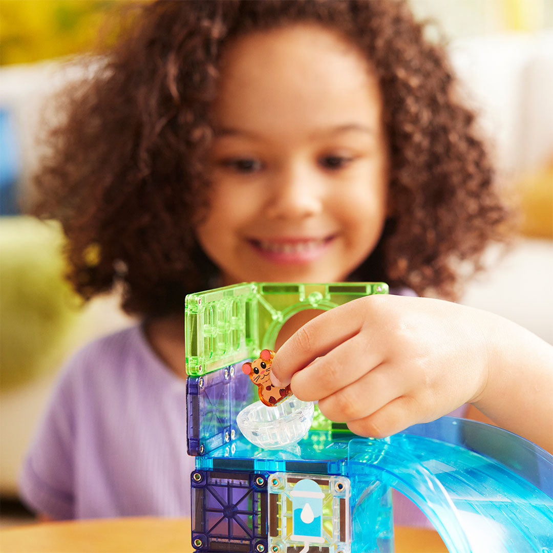 Een kind plaatst het hamsterfiguur in de transparante bal op de Magna-Tiles Hamster Ball knikkerbaan.