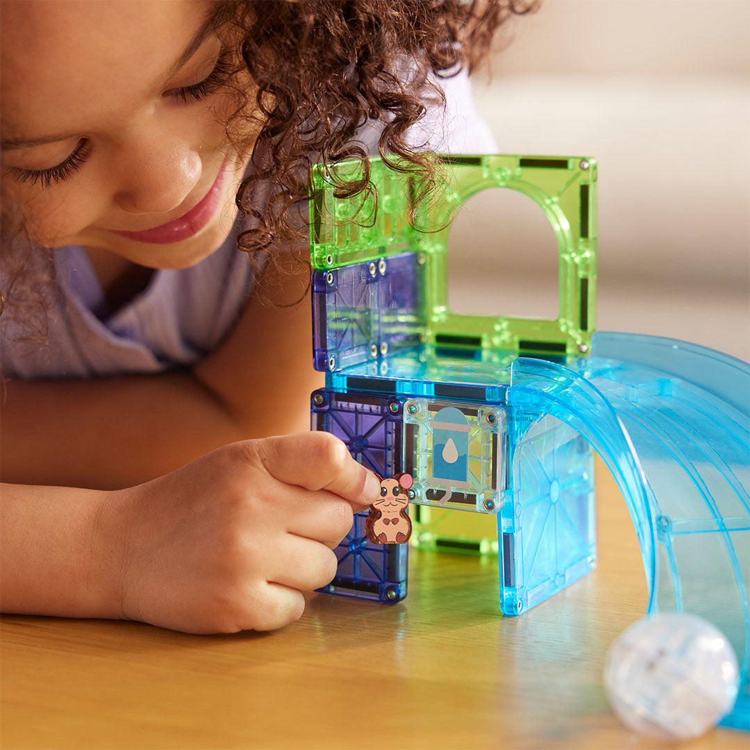Een kind plaatst het hamsterfiguur in de Magna-Tiles Hamster Ball knikkerbaan van magnetische tegels.