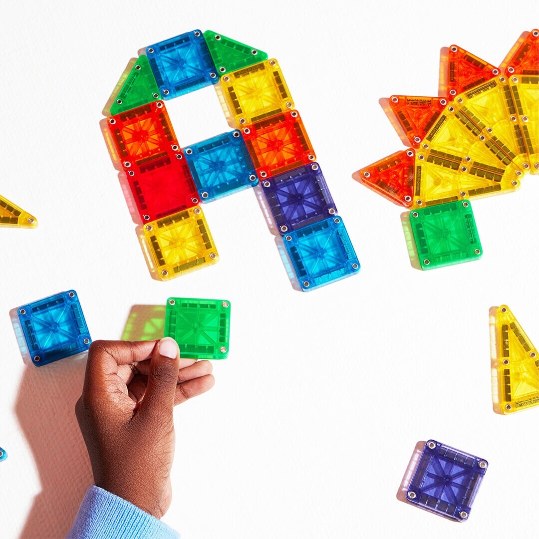 Een hand plaatst een groene Magna-Tiles Micro Mags tegel naast andere tegels die de letter A vormen.