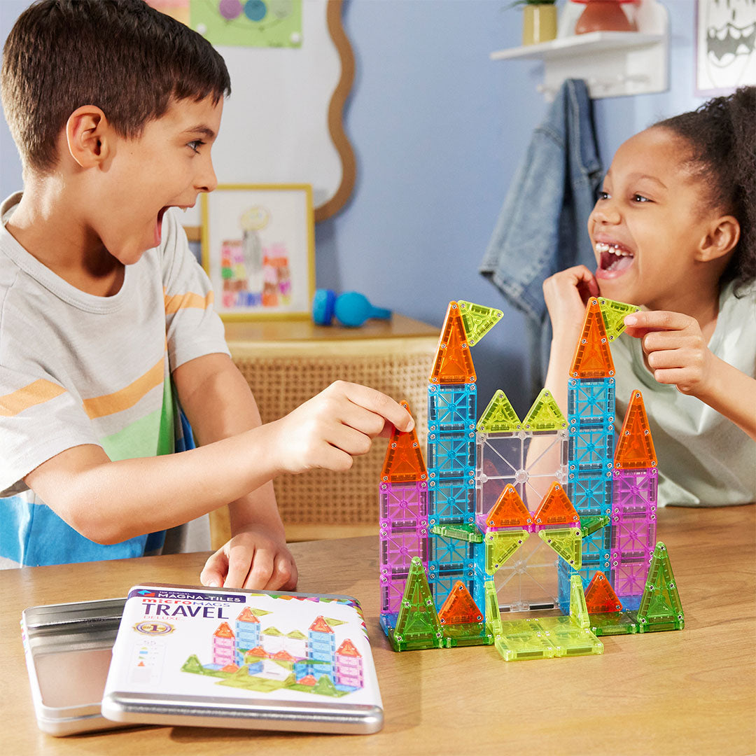 Twee lachende kinderen bouwen een kleurrijk kasteel met Magna-Tiles magnetische tegels.