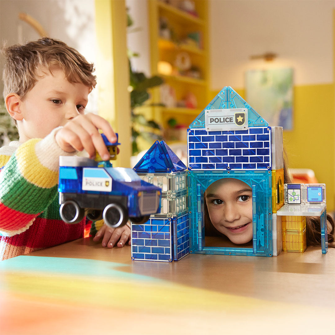 Een kind speelt met de Magna-Tiles politiebureau bouwset, waarbij een meisje door de deur van het politiebureau kijkt.