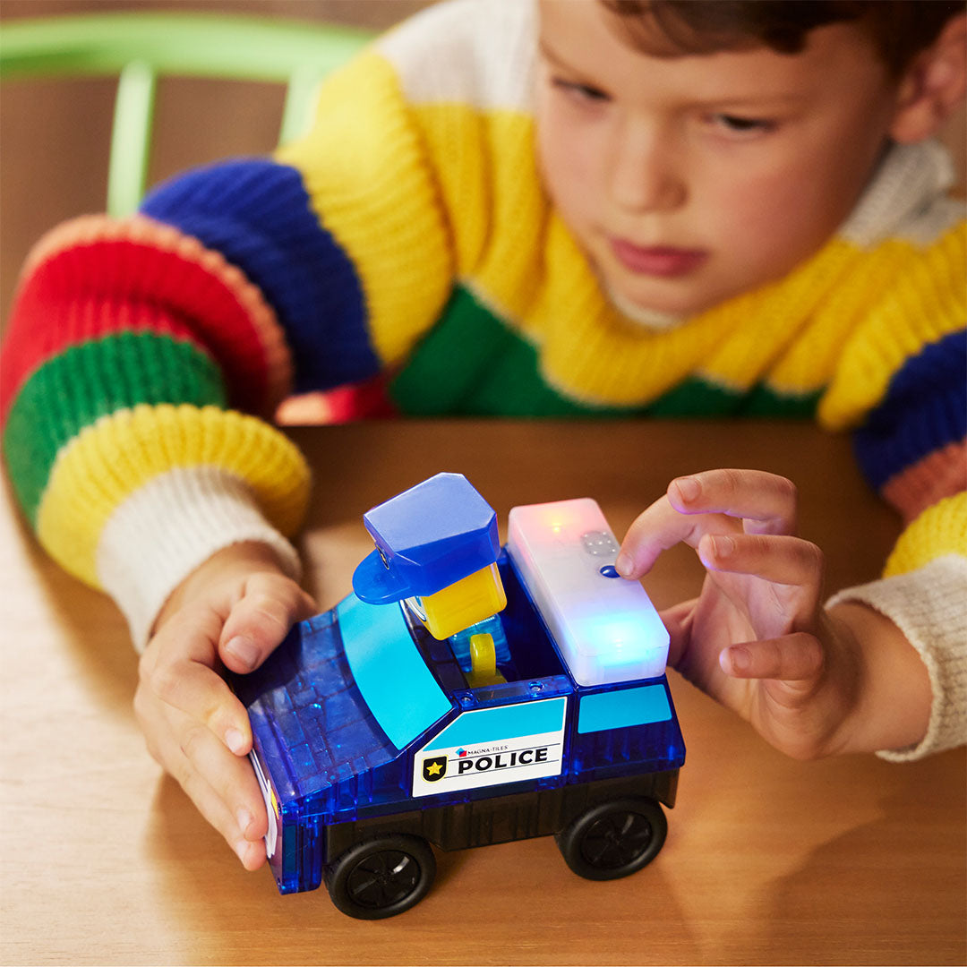 Een kind drukt op een knop op de Magna-Tiles politieauto, waardoor de zwaailichten oplichten.