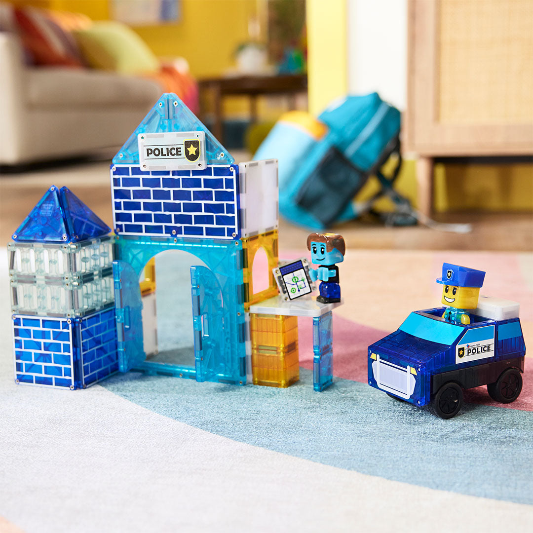 De Magna-Tiles politiebureau bouwset met een blauw politiebureau, een politieauto en twee figuren op een vloerkleed.